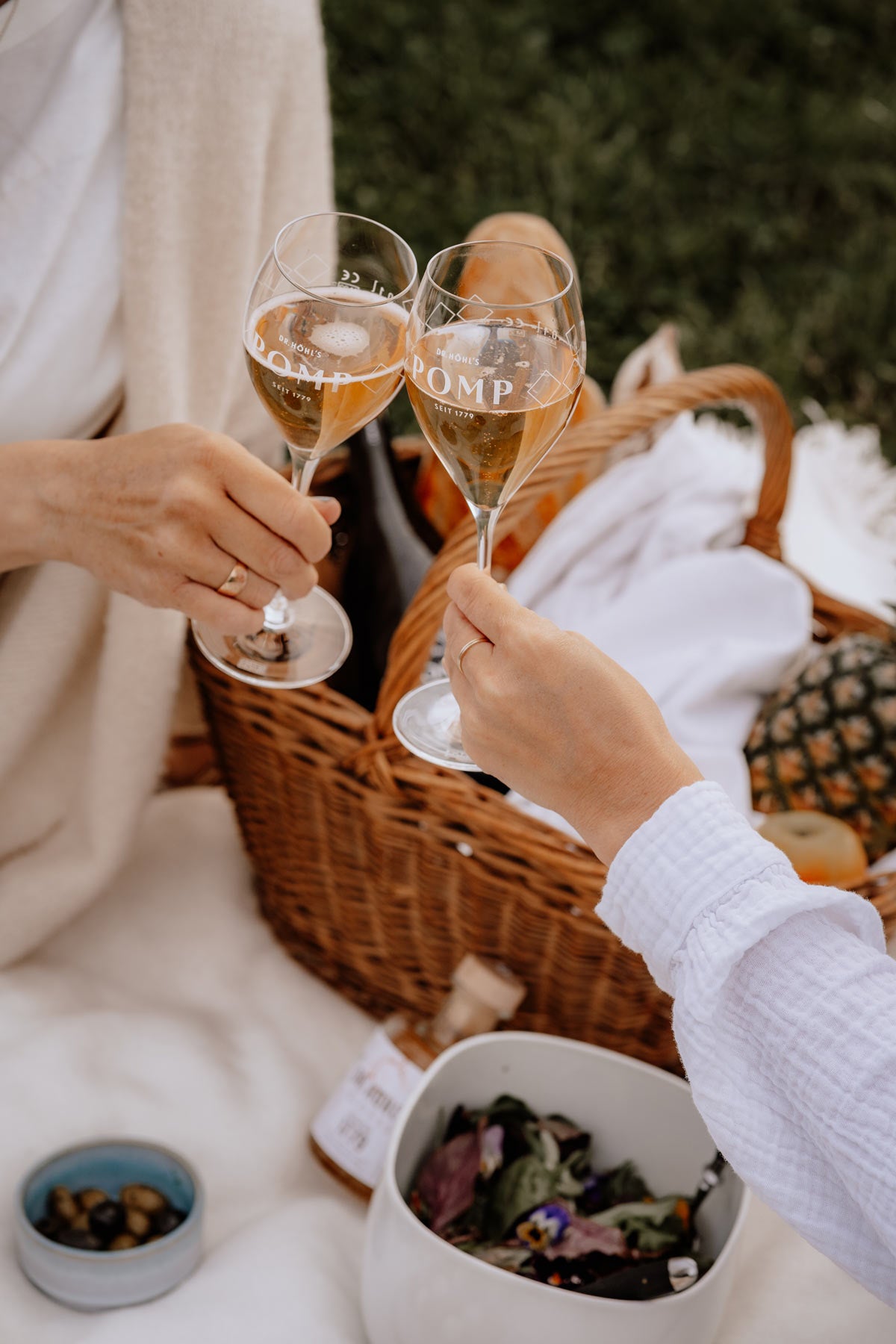 zwei pomp champagner gläser die sich zum anstoßen über einem picknick korb treffen