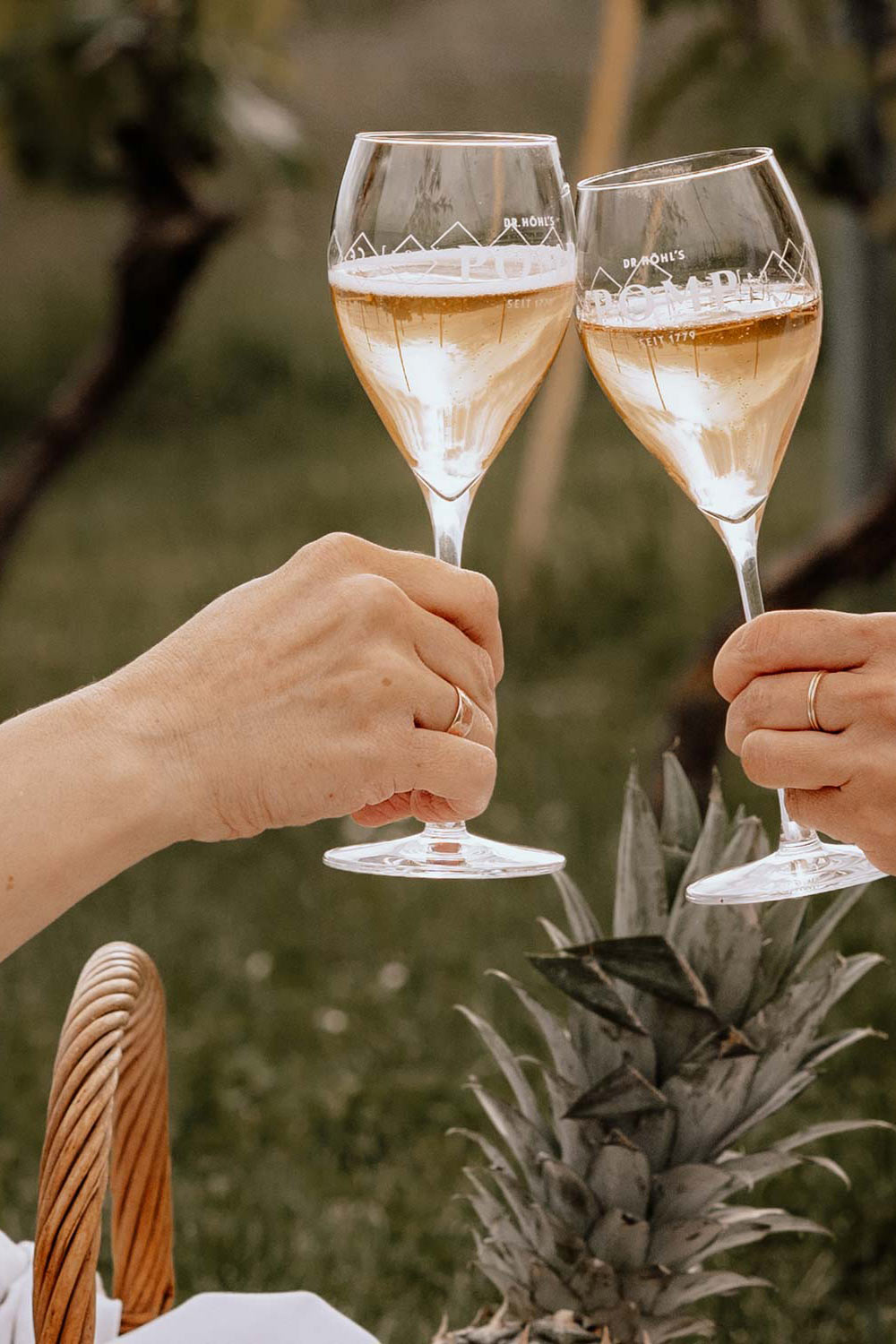 zwei hände stoßen mit pomp alkoholfrei gefüllten champagnergläsern an