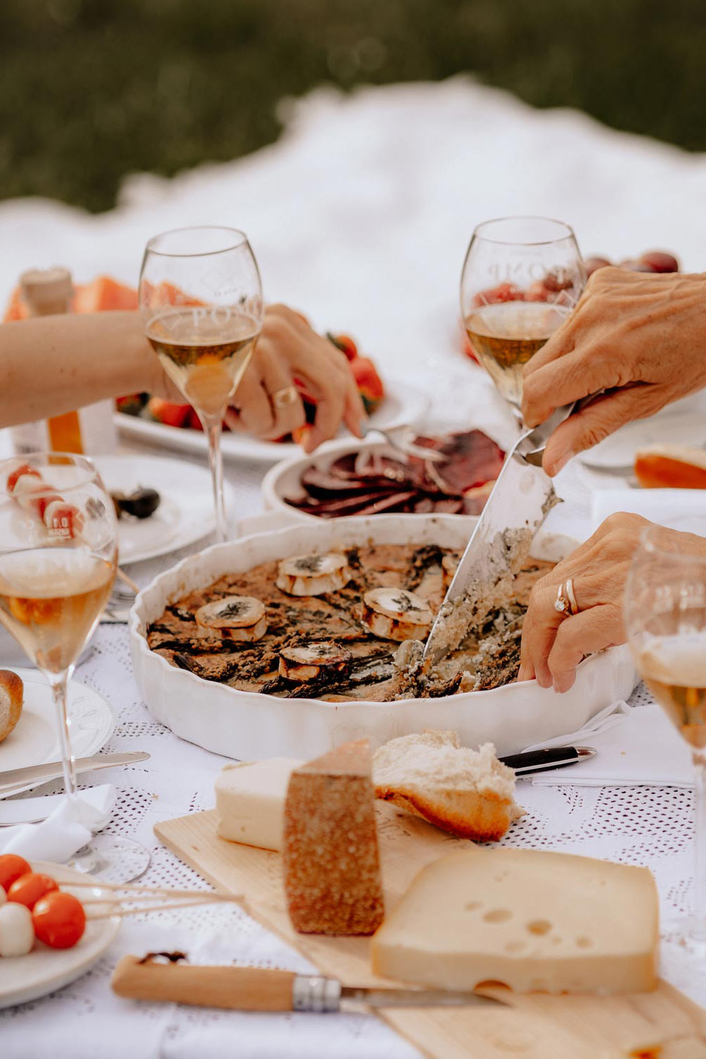 quiche, pomp sektgläser und andere leckereien auf einem weiß eingedeckten picknick tisch
