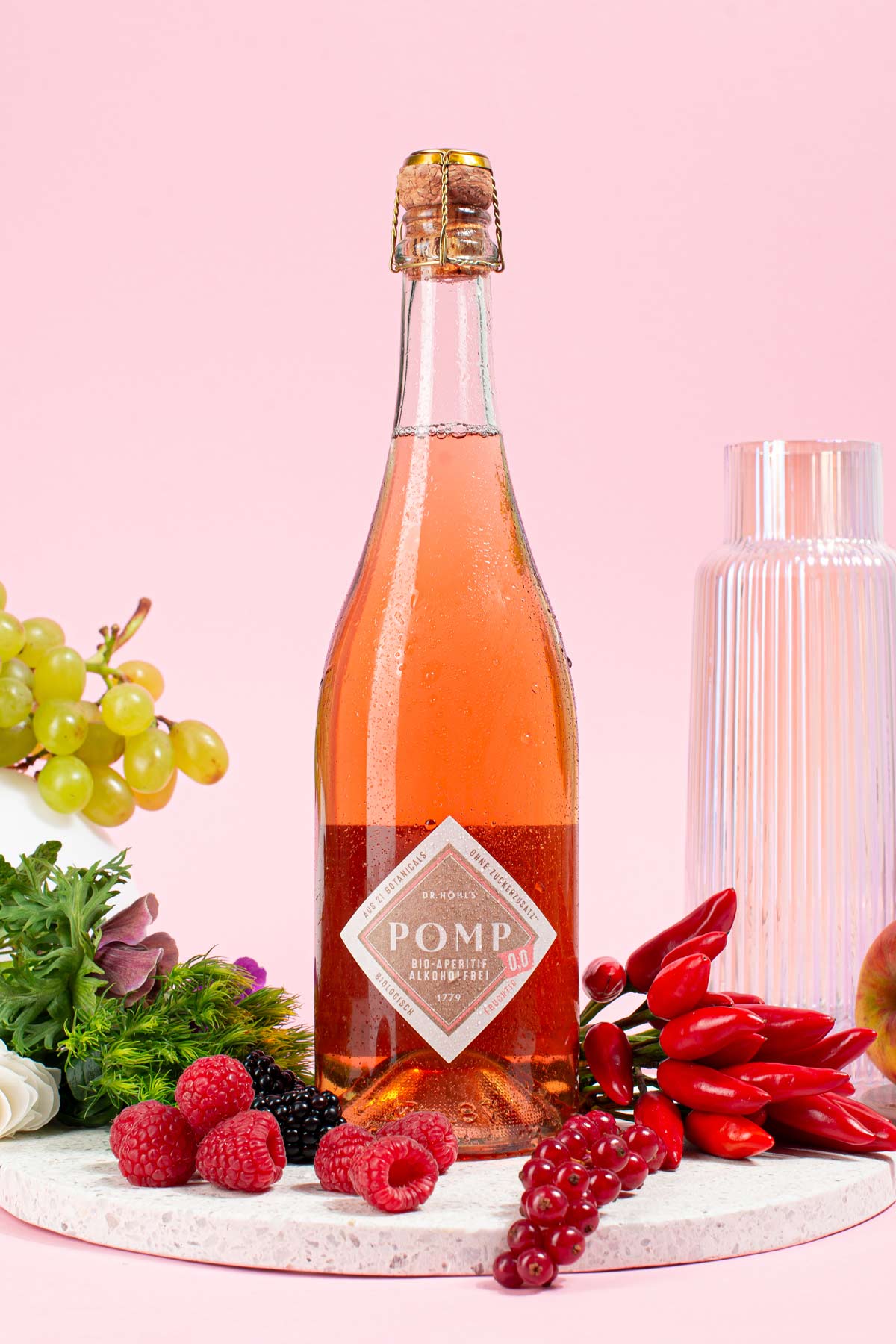 flasche pomp 0,0 fruchtig alkoholfrei auf einem steintablett zwischen zutaten wie chilis beeren trauben und apfel