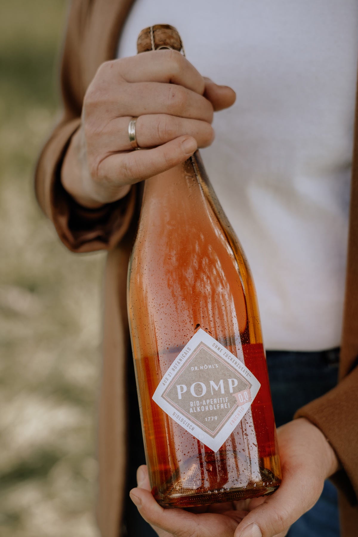 dana steht auf der streuobstwiese und hält eine flasche alkoholfreien sekt in ihren händen