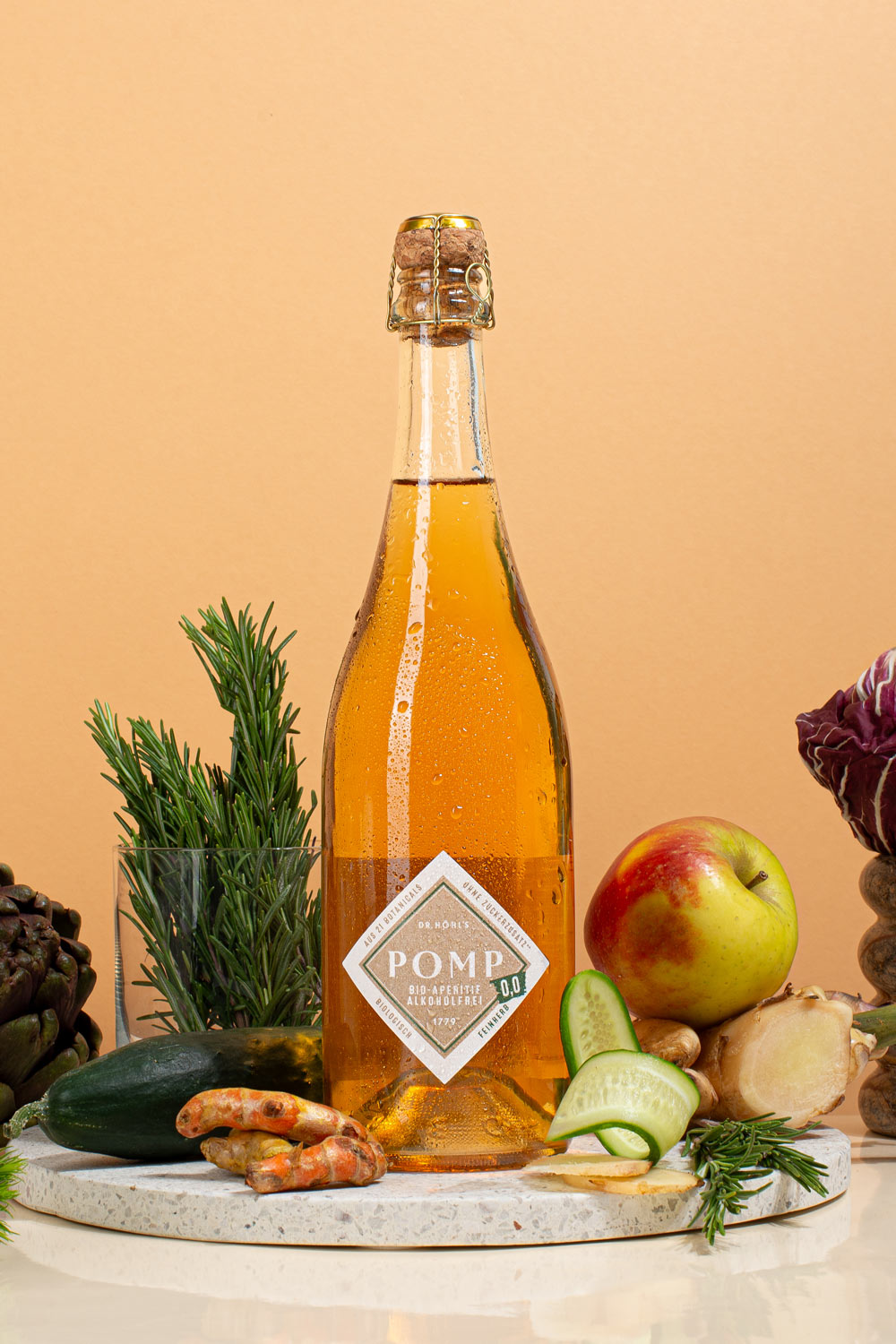 eine flasche eisgkühlter alkoholfreier aperitif auf einem steintablett mit frischen zutaten wie apfel gurke kurkuma und ingwer dekoriert