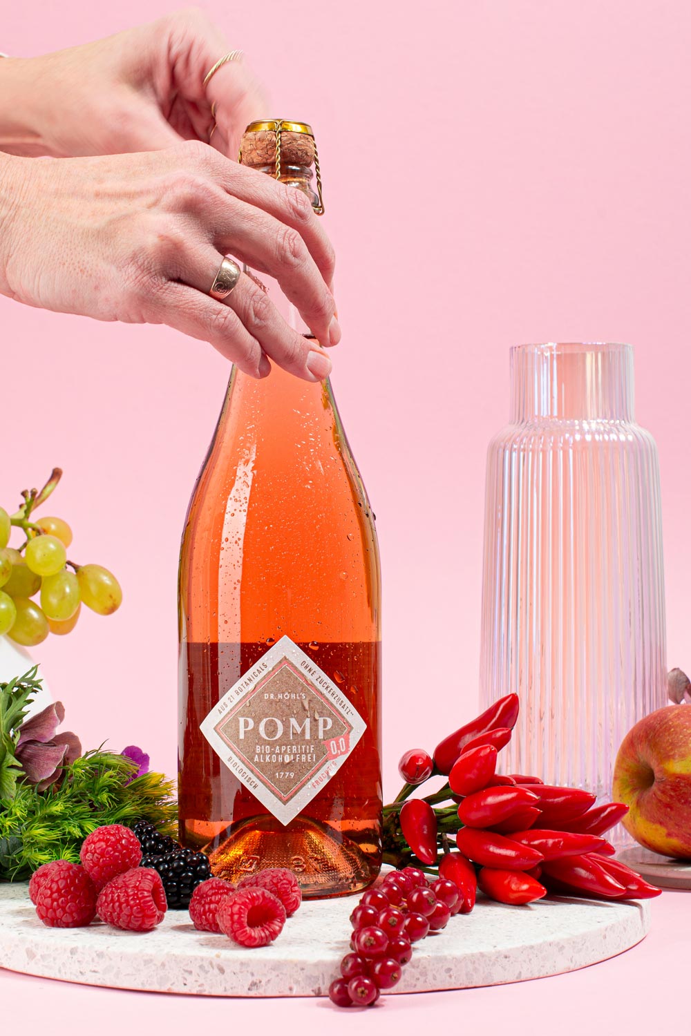 frau öffnet eine flasche rose aperitif 0,0 der auf einem weißen tablett mit frischen zutaten steht