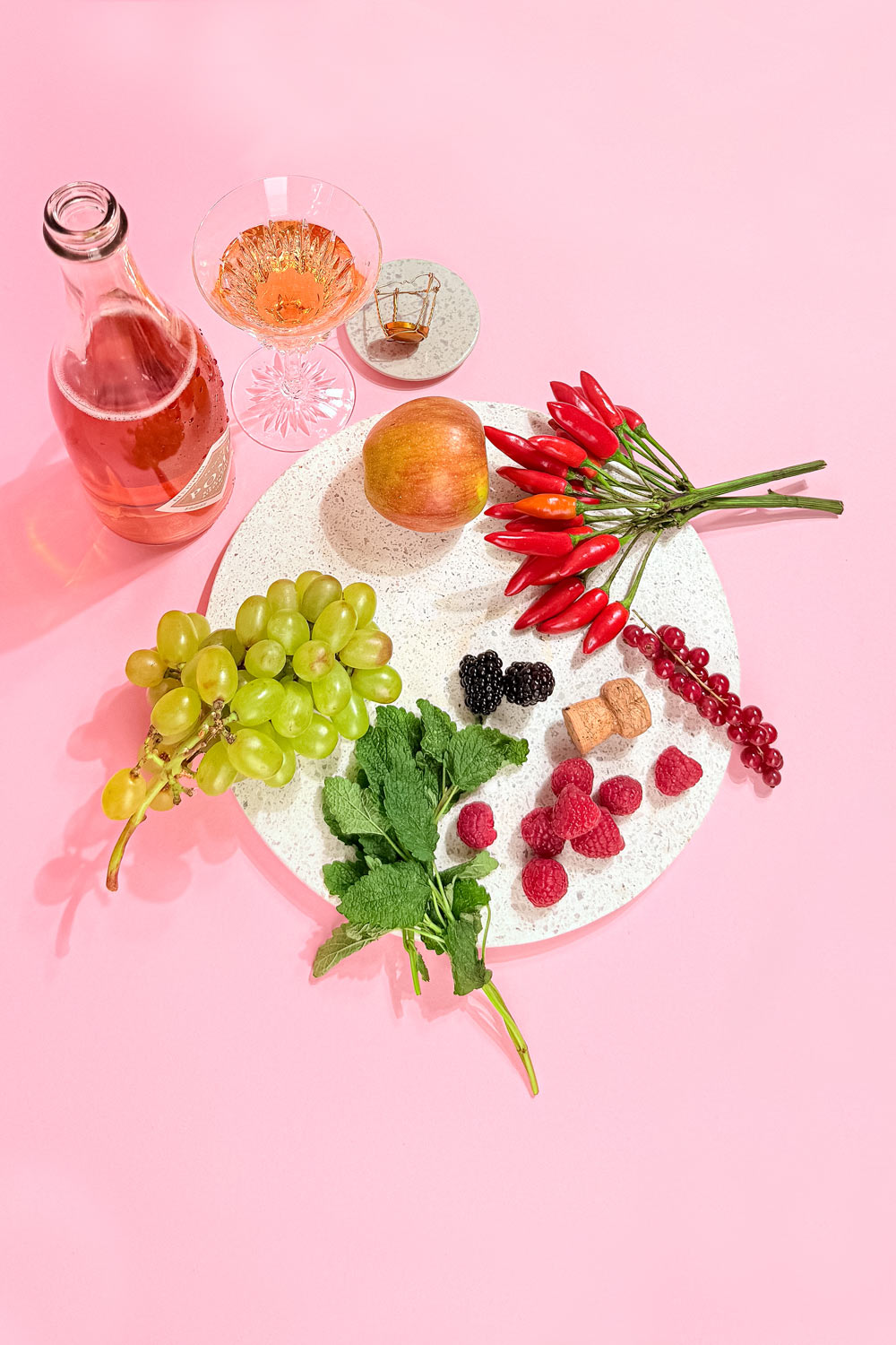 apfel, trauben, chili, melisse und weitere frische zutaten auf einem steintablett neben einer flasche alkoholfreiem aperitif und einem kristallglas von oben fotografiert