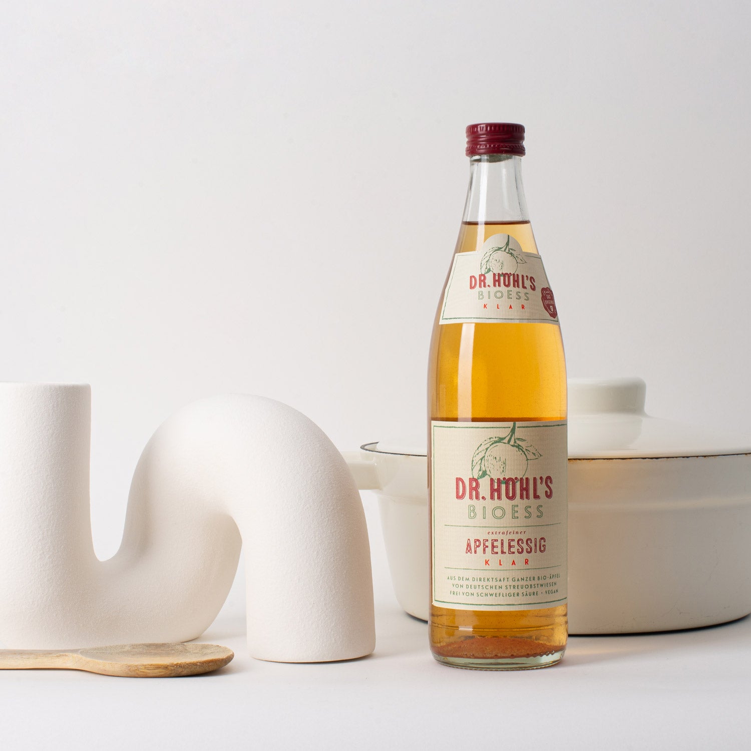 helles stillleben einer flasche bio-veganer apfelessig bioess, einem porzellan darm, kochlöffel sowie einem kochtopf