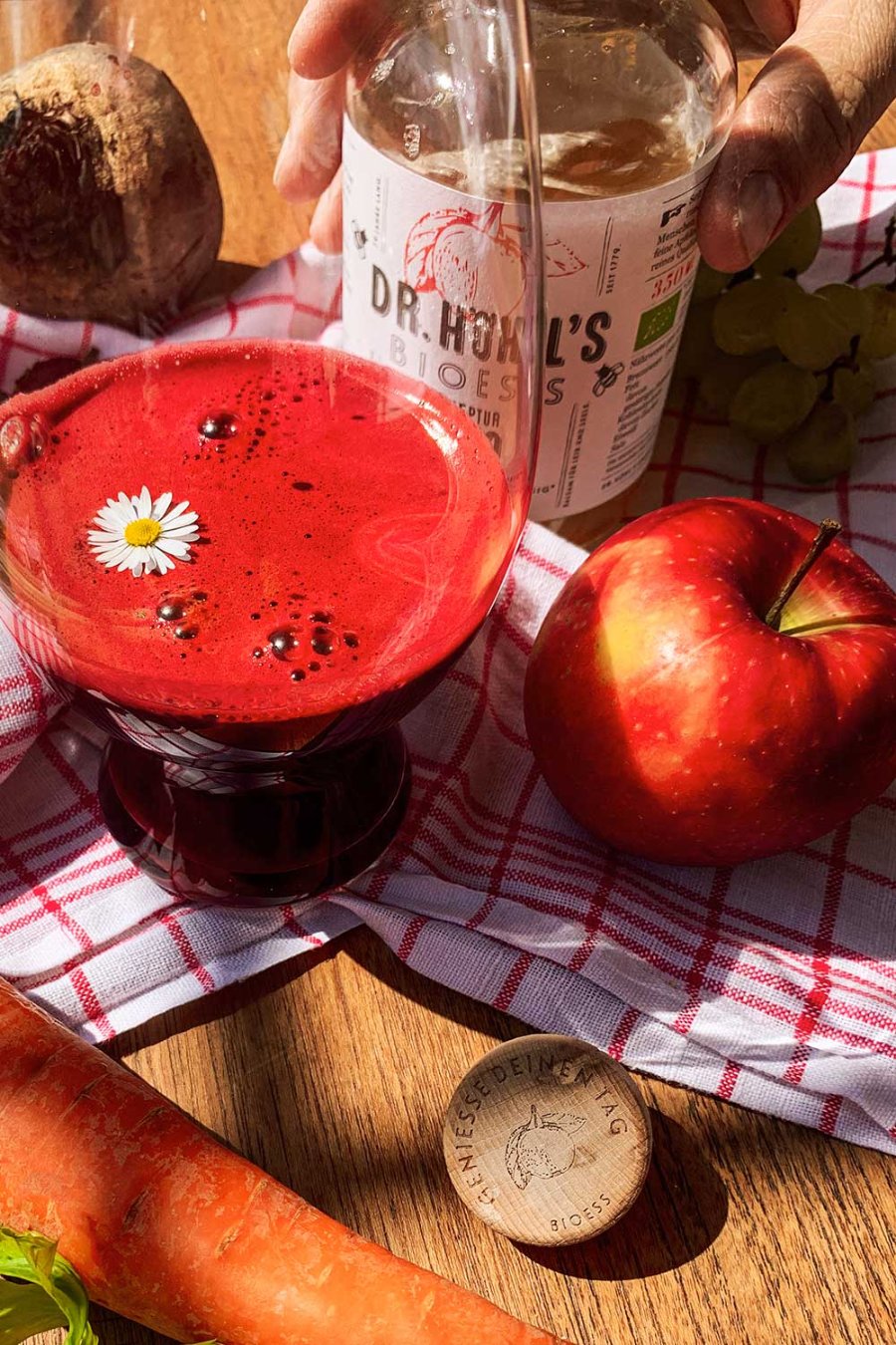 close up rote beete smoothie in einem glas mit gänseblümchen und apfel dekoriert neben einer flasche rezeptur 1779