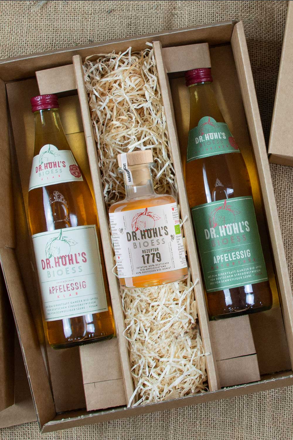 aufgeklappte geschenkbox mit holzwolle und 3 gourmet essigen gefüllt