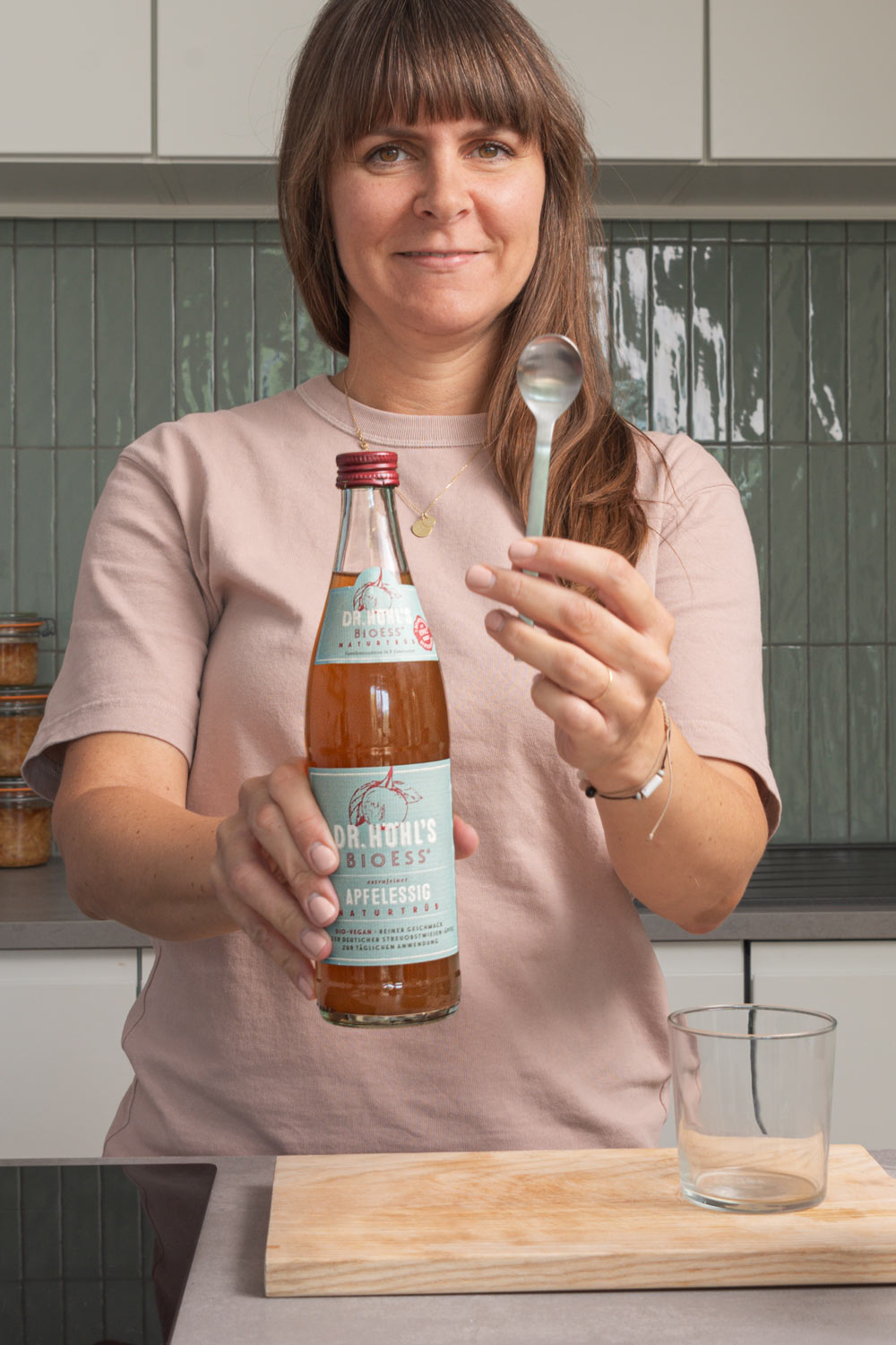 Anna hält einen Löffel und eine Flasche naturtrüben Apfelessig in die Kamera