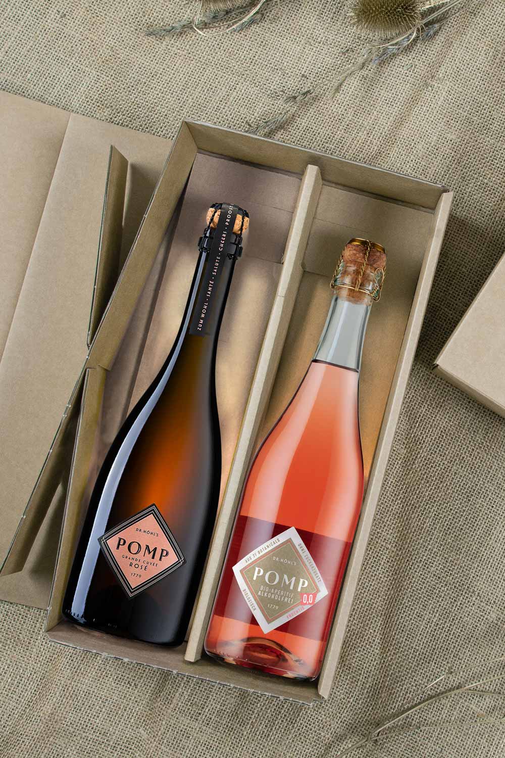 blick in aufgeklappte geschenkbox aus naturkarton mit einer schwarzen design flasche pomp rose und einer flasche pomp bio-aperitif 0,0 alkoholfrei