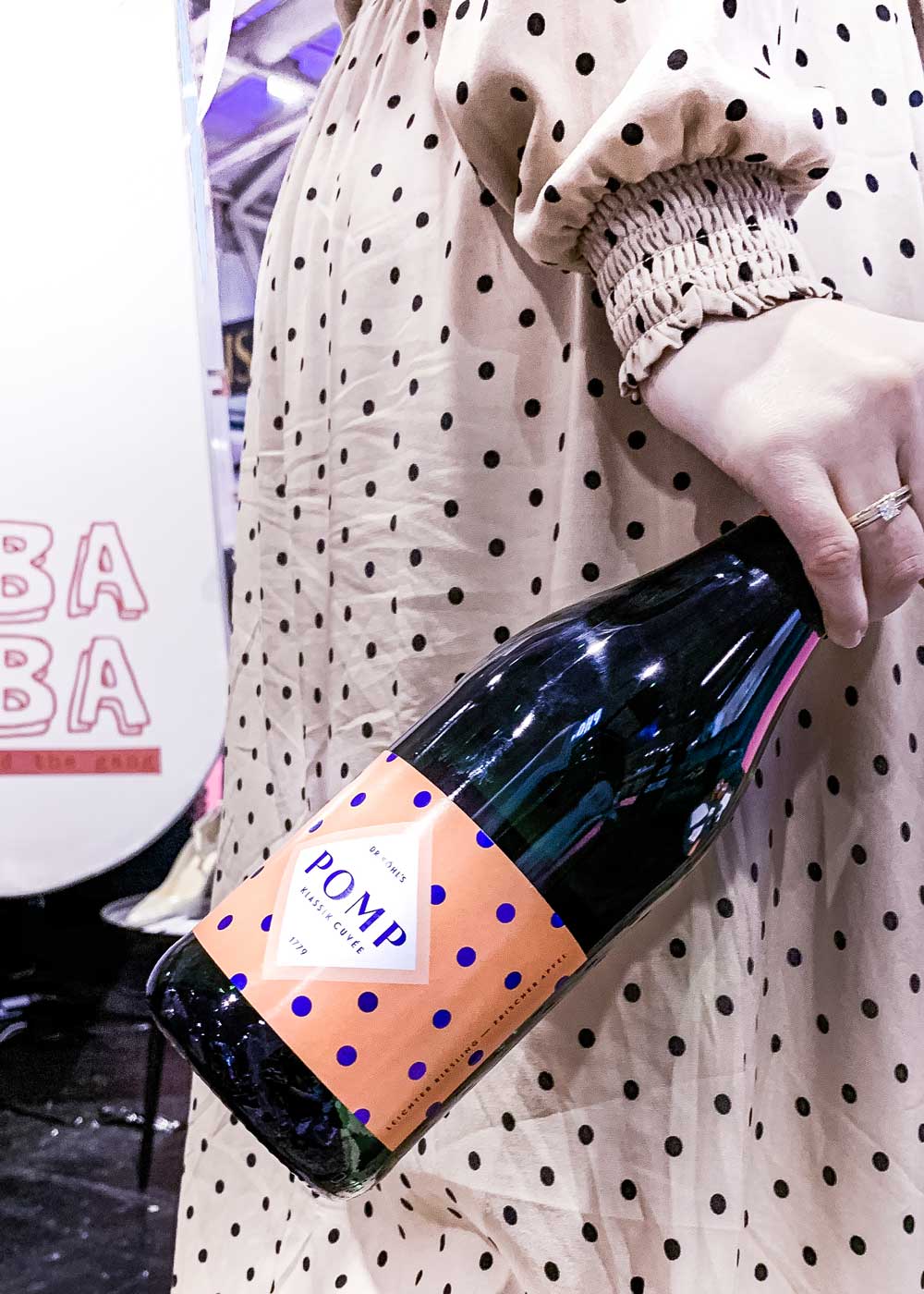 close up sektflasche im dots design in der hand einer frau mit polka dots kleid