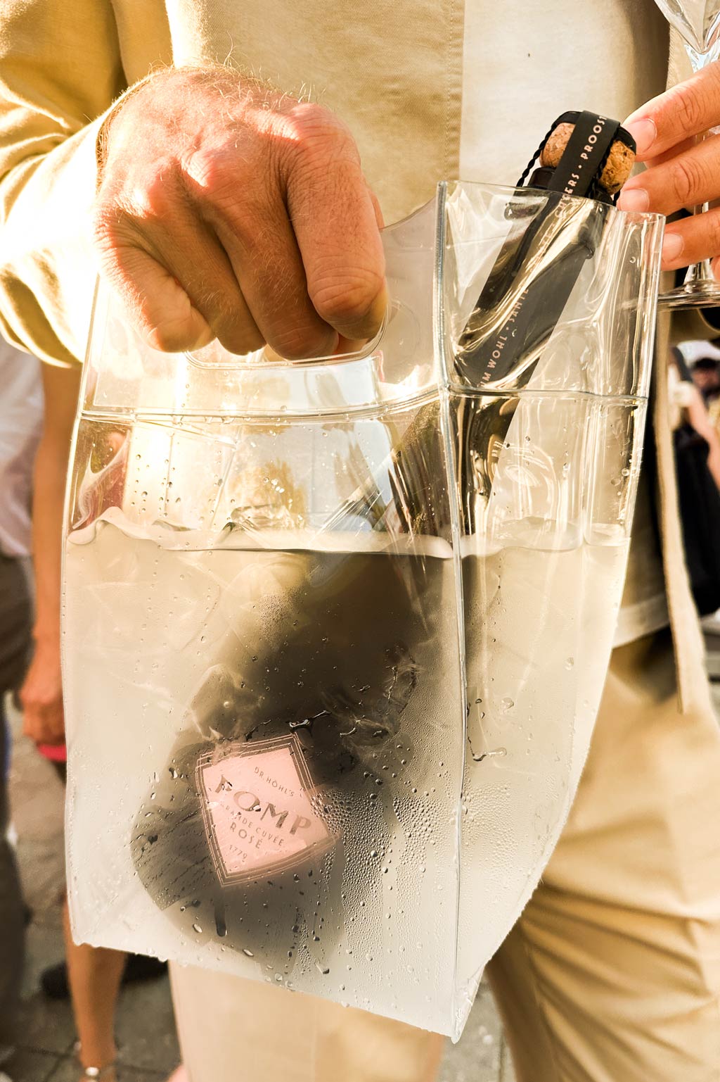 Flasche POMP Sekt im Icebag getragen von einem Mann in cremefarbenem Outfit