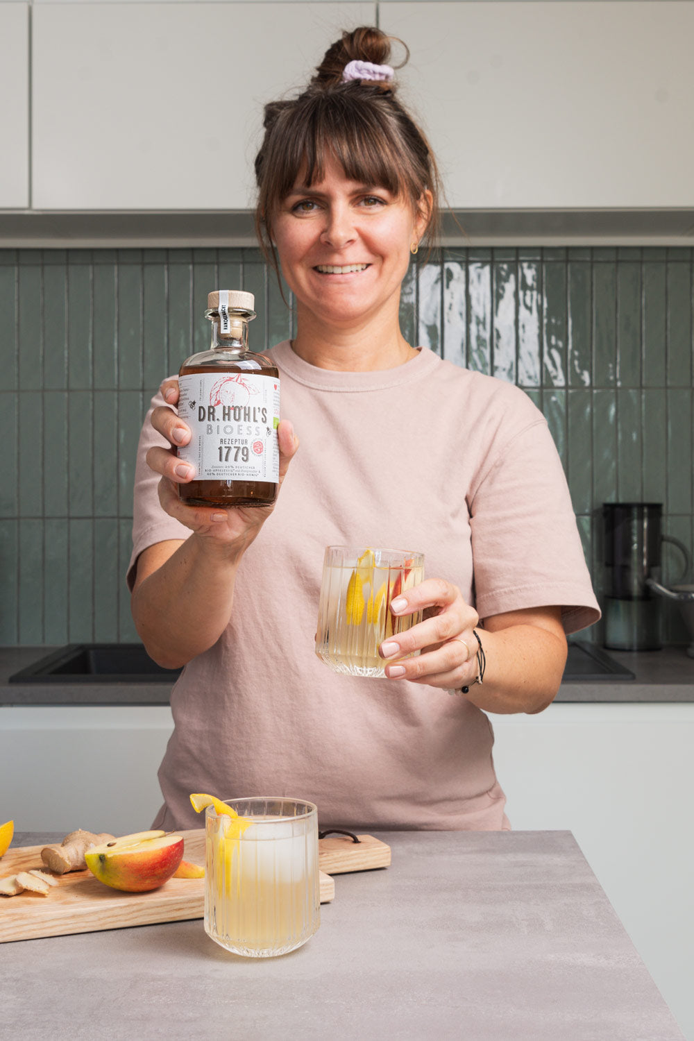 Anna hält eine Flasche Apfelessig Honig Rezeptur und ein Glas frische Apfelessig Limonade in den Händen
