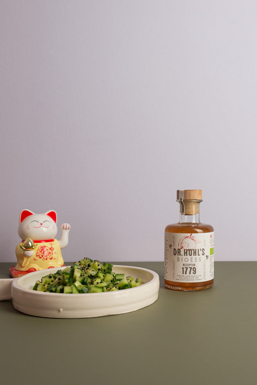 asiatischer Gurkensalat mit einer Flasche Apfelessig Honig Mischung neben einer Winkekatze