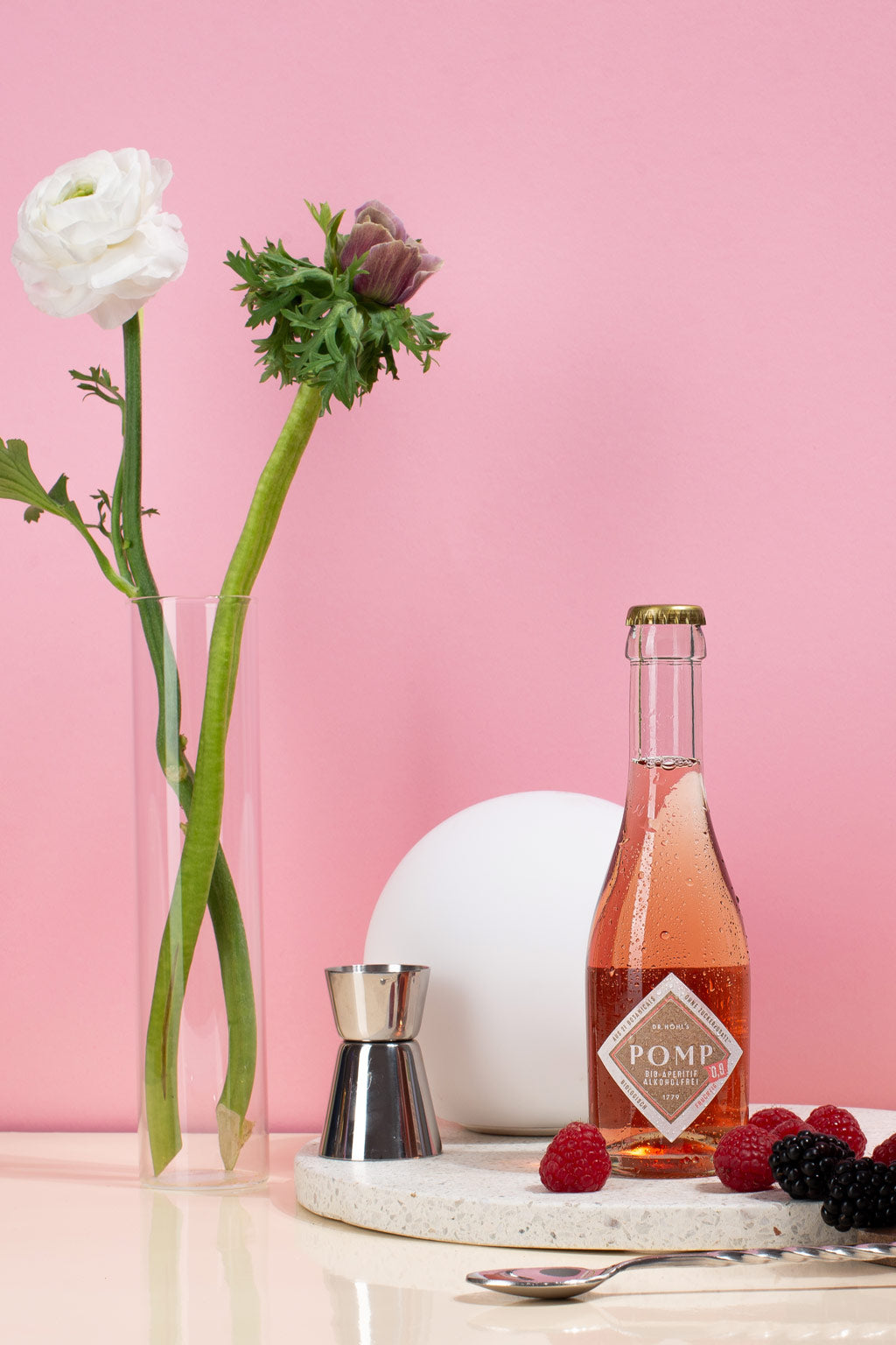 Piccolo alkoholfreier Sekt rosé neben Blumen und frischen Beeren