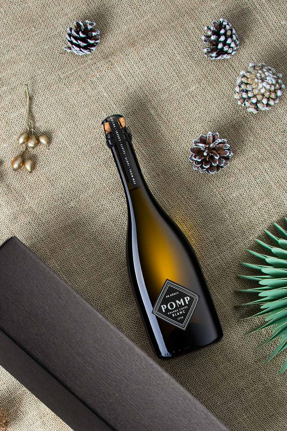flasche pomp blanc sekt neben schwarzer geschenkbox auf weihnachtlichem hintergrund und deko