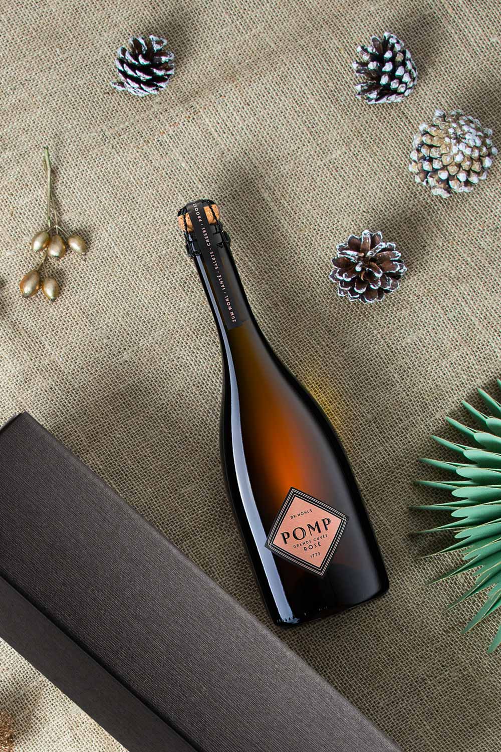 flasche pomp rosé sekt neben schwarzer geschenkbox auf weihnachtlichem hintergrund und deko