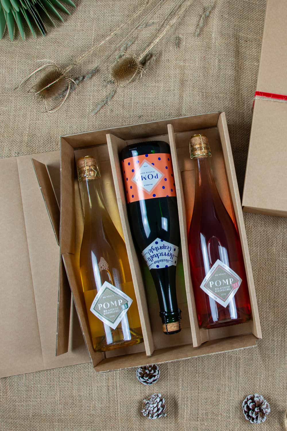 aufgeklappte geschenkbox mit 3 flaschen sekt auf weihnachtlichem dekohintergrund