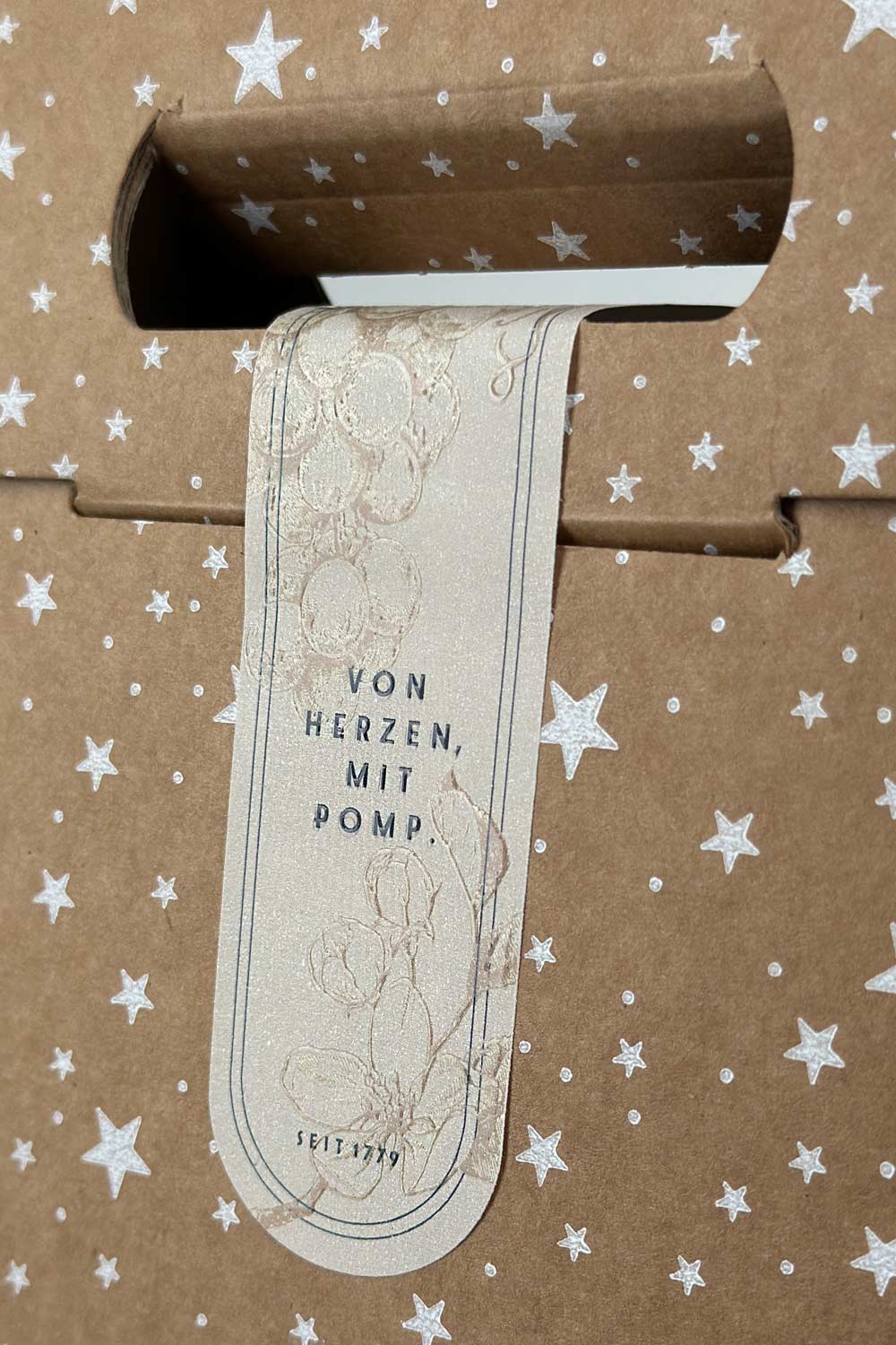 veredelte banderole mit der aufschrift "von herzen mit pomp" auf einer naturkarton geschenkbox mit tragegriff
