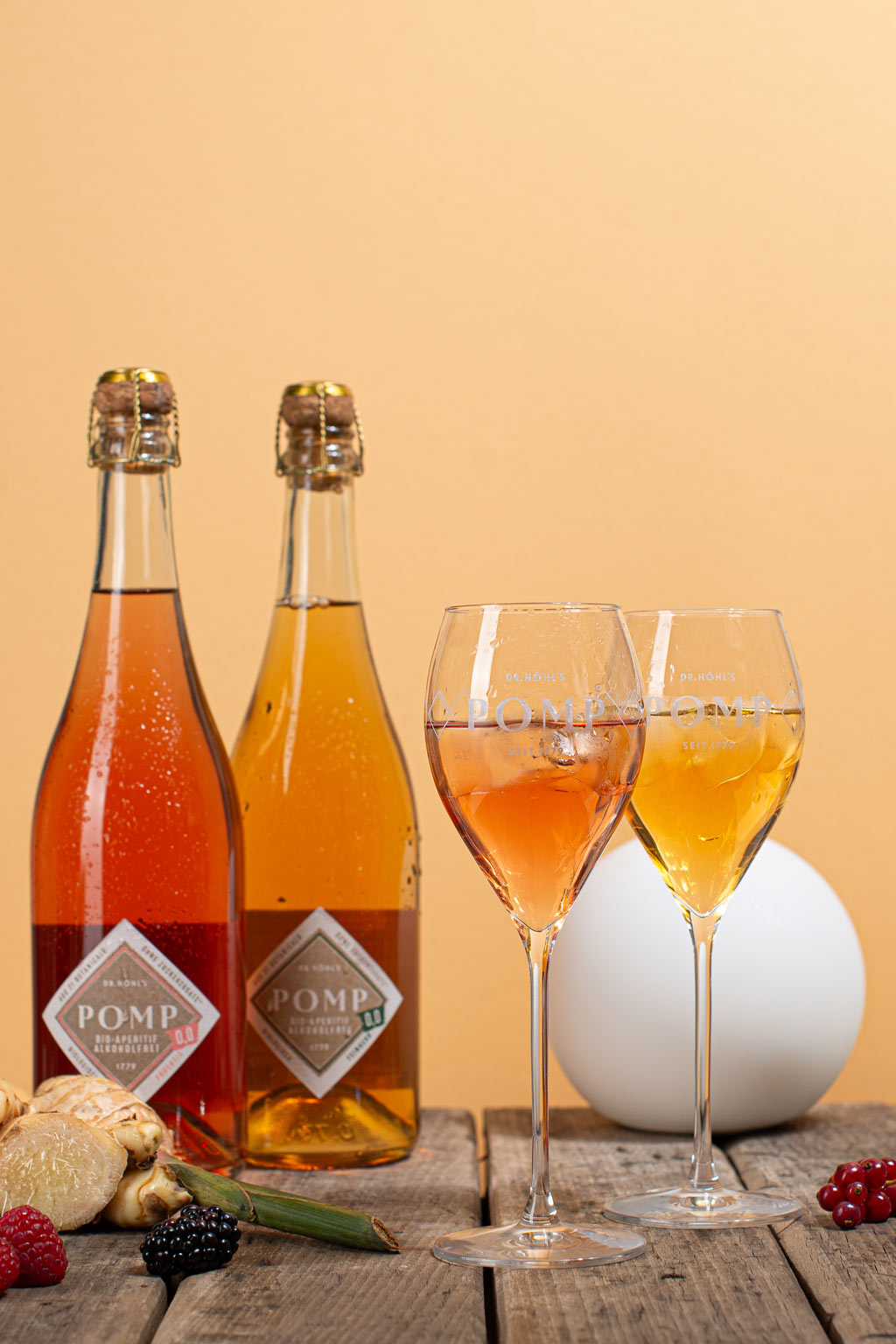 zwei sektgläser gefüllt mit zwei sorten feinem alkoholfreiem aperitif vor zwei flaschen pomp 0,0