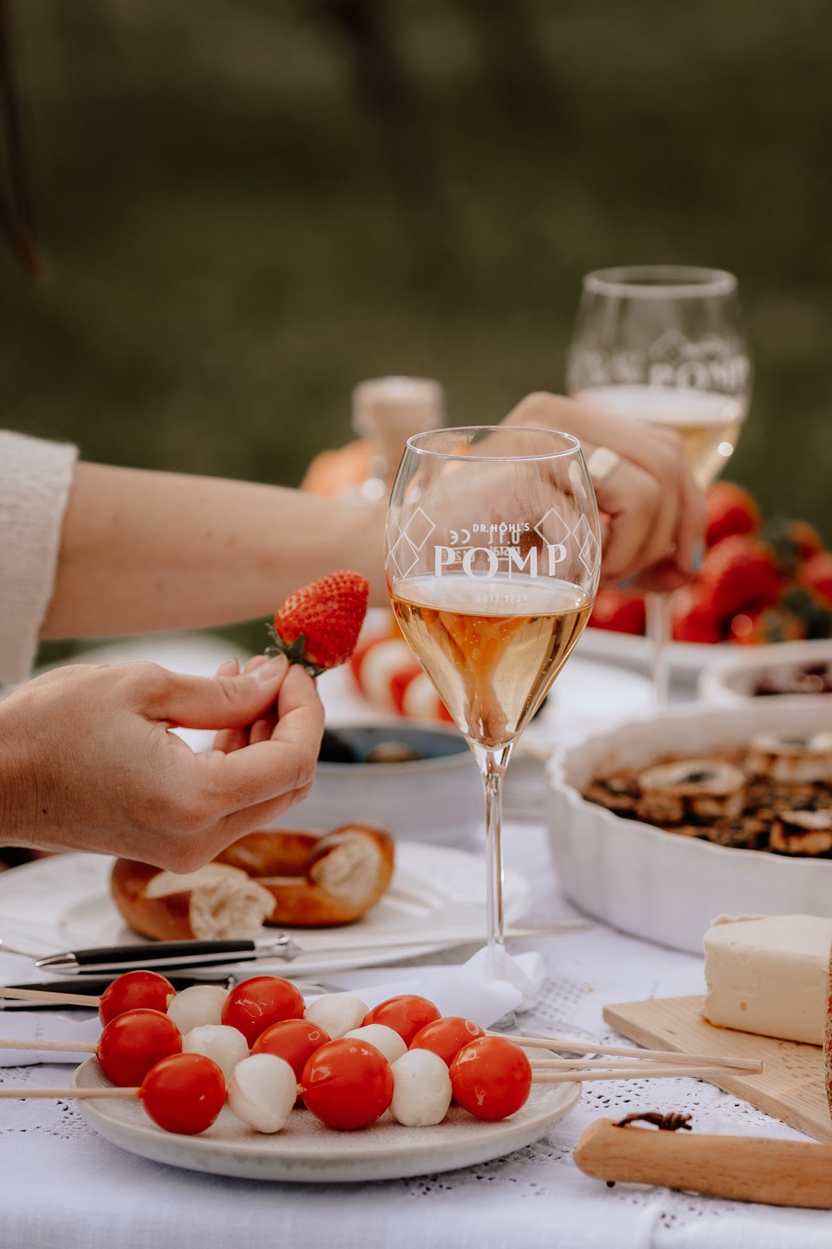 white picknick tisch gedeckt mit quiche tomatensticks und champagnergläsern mit pomp logo