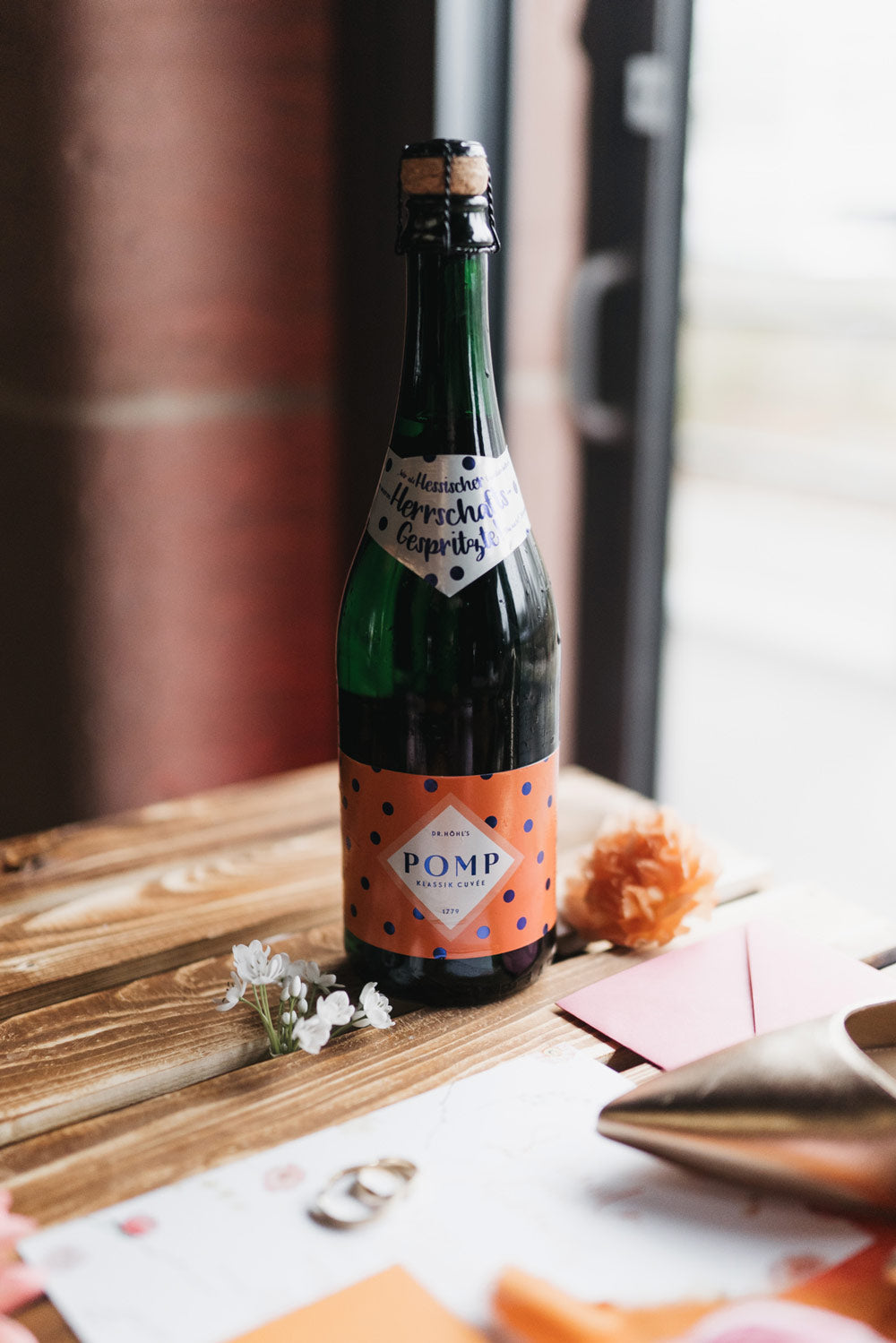 Sektflasche mit orangefarbenem Etikett mit blauen Punkten auf einem Holztisch mit Hochzeitsdeko