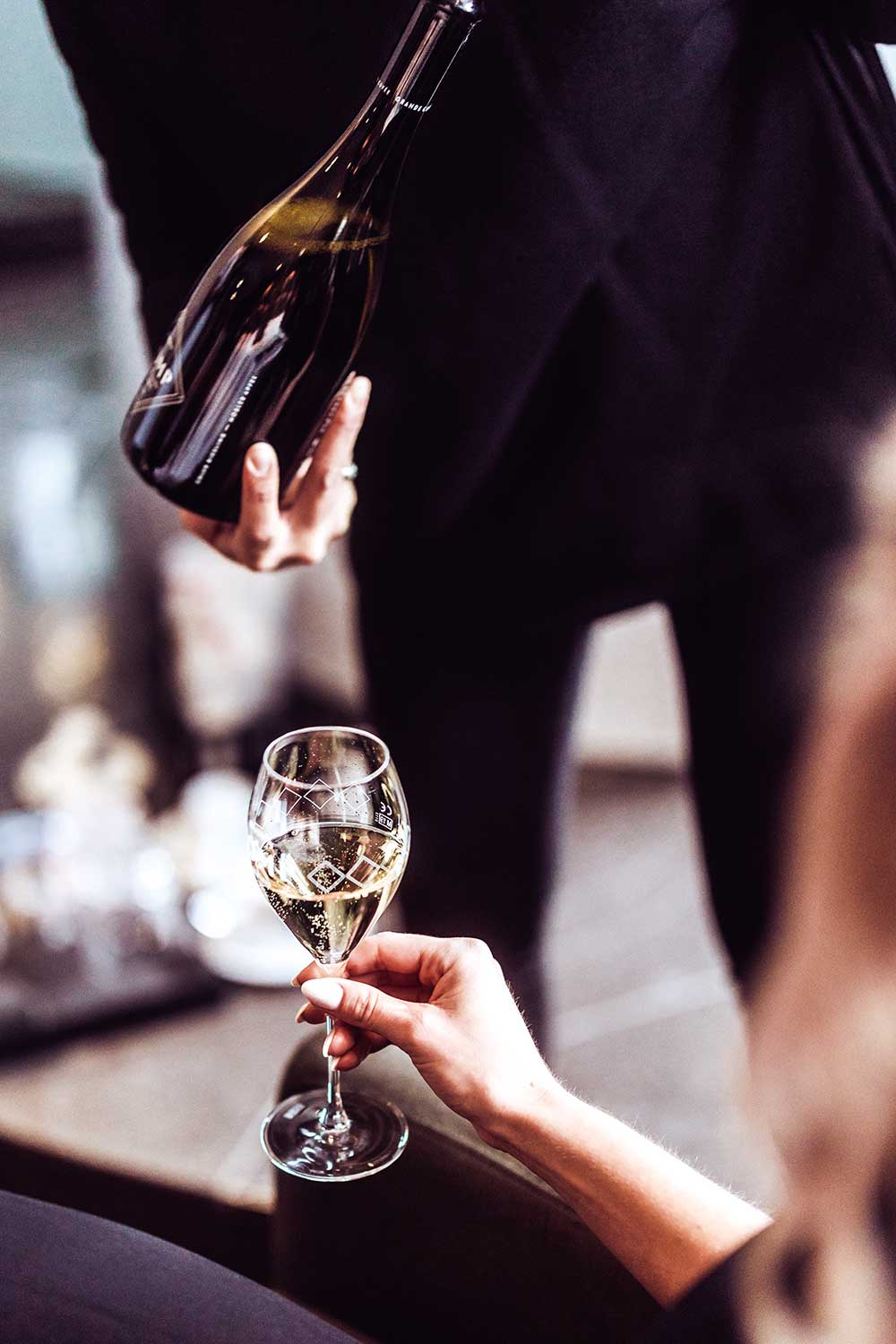 frau hält champagnerglas zum einschenken unter die flasche