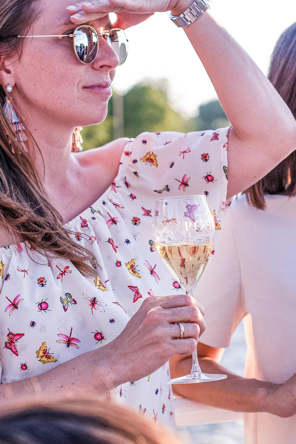 frau im sommerkleid mit einem glas kalten sekt in der hand schweift in die ferne