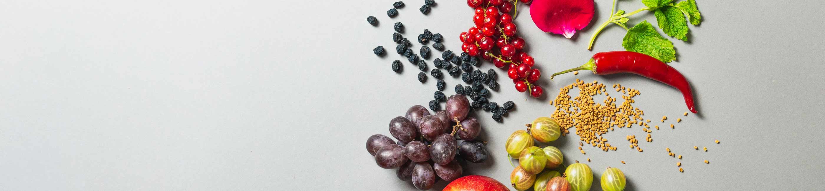 bio-aperitif zutaten stillleben mit trauben, beeren, rosen, melisse, chili, bockshornklee und stachelbeeren