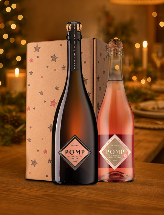 zwei flaschen rose sekt mit einer weihnachtsgeschenkbox stehen auf einer festlich gedeckten weihnachtstafel