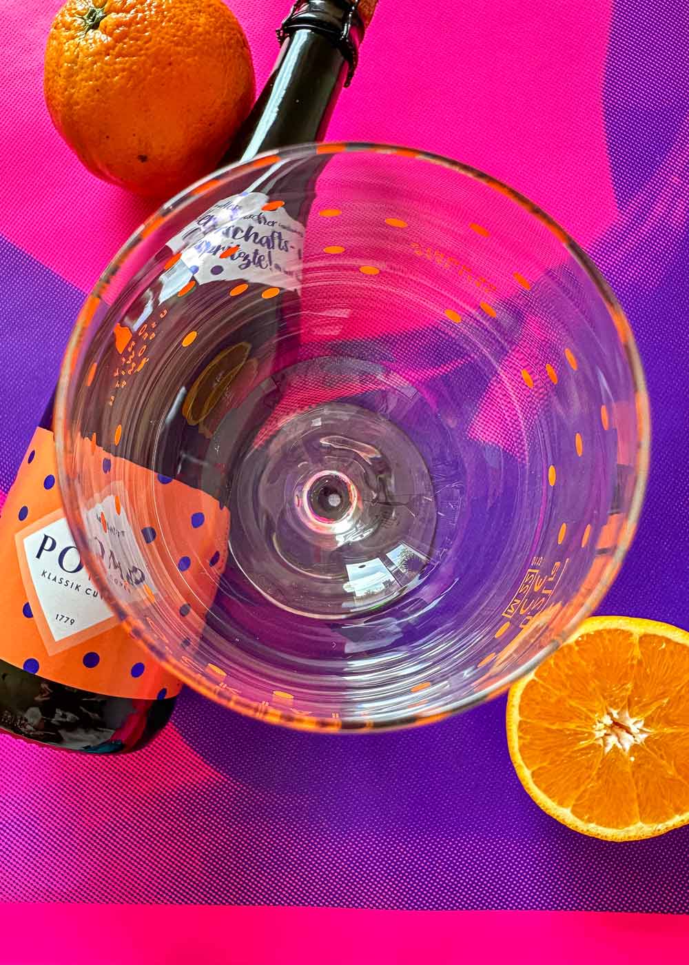 draufsicht von einem glas für aperol spritz mit pomp sektflasche und orange als deko