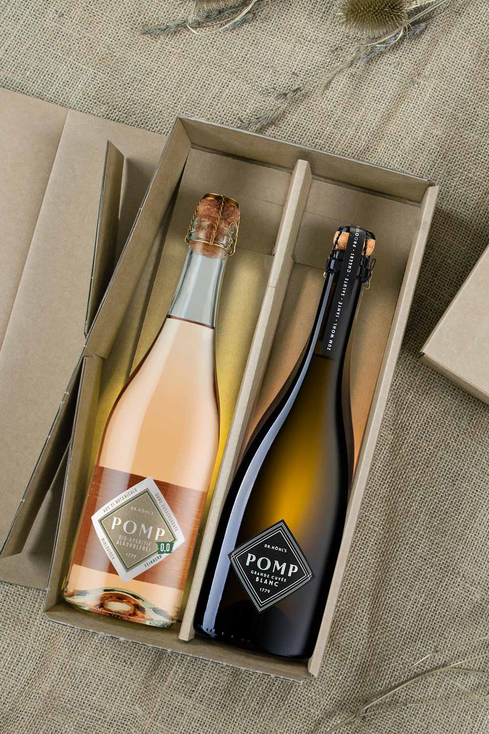 Blick in die Geschenkbox natur mit einer flasche bio apero alkoholfrei und einer schwarzen flasche sekt pomp blanc