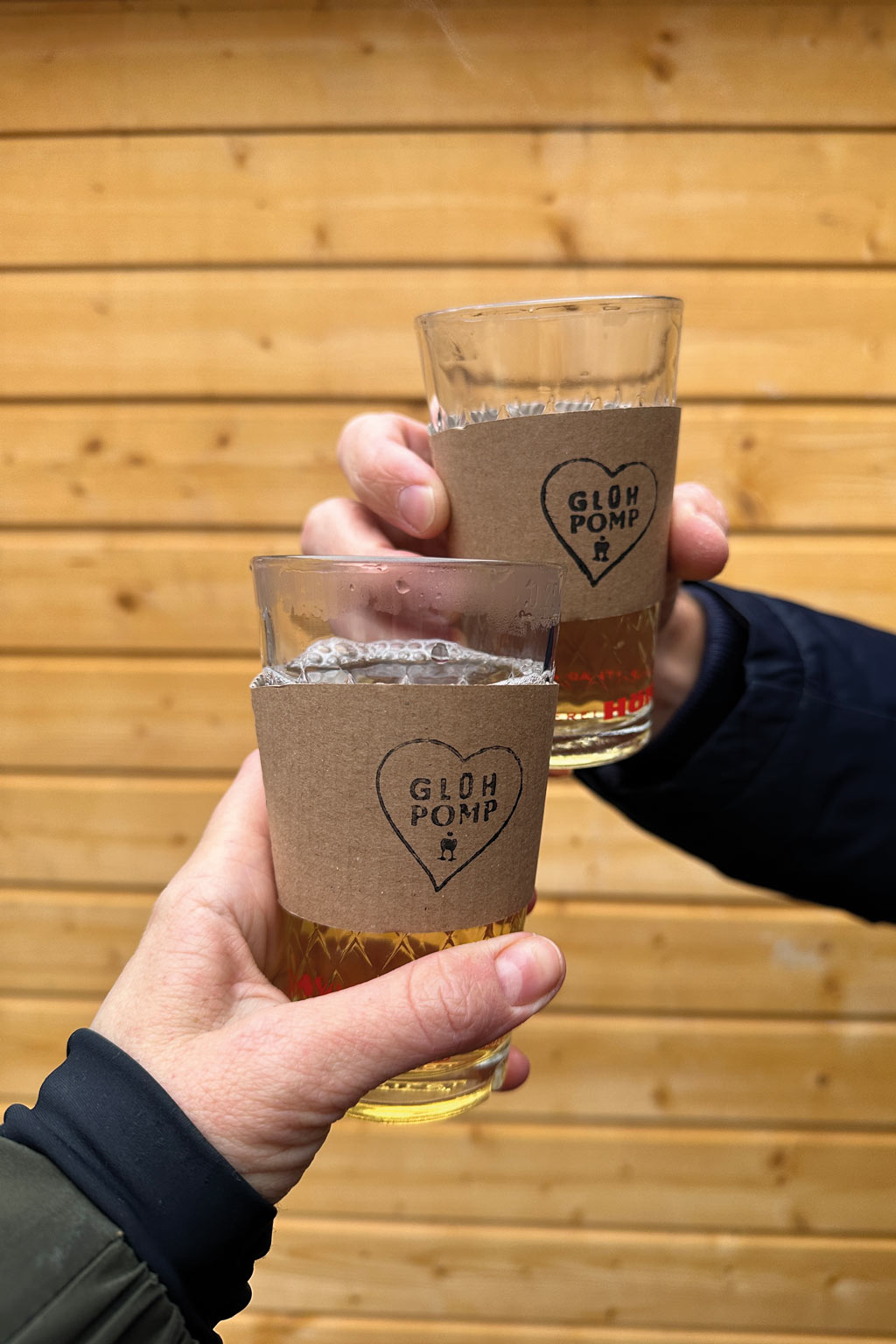 zwei becher mit glüh pomp manschette und heißem glühwein vor einer holzwand