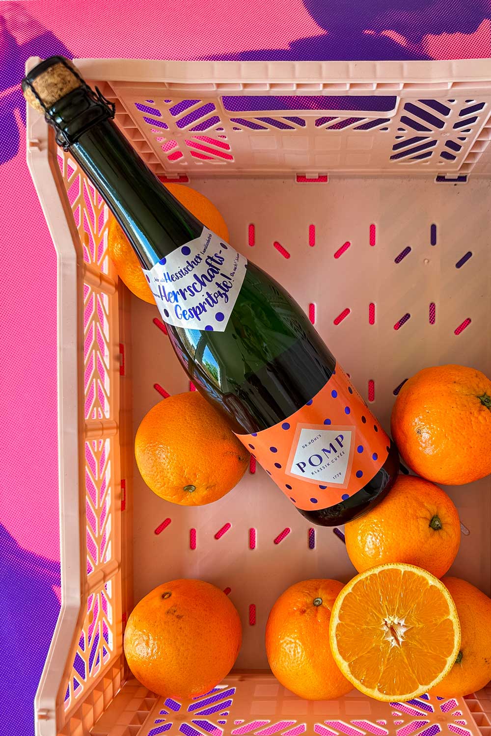 flasche pomp sekt mit orangenem etikett in einer rosa kunststoff-kiste mit einigen orangen